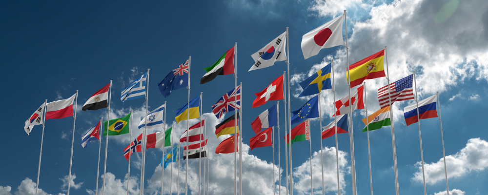 Various country flags flying against a blue sky